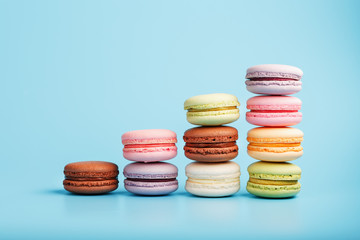 Macaroni cookies of different colors are arranged in the shape of pyramid steps on a blue background.