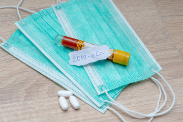 Medical face mask and pills with inscription Wuhan coronavirus 2019-nCoV on yellow table background. Novel coronavirus COVID-19 concept.