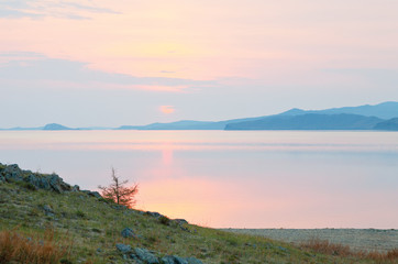 Beautiful calm landscape of a spring early morning on the shore of Baikal Lake at dawn. Natural background, pastel pink and golden natural colors