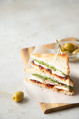 Sandwich with chicken breast, dried tomatoes, mozzarella and pesto with olives on background.