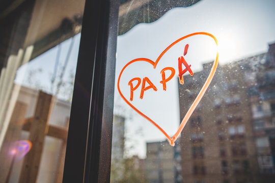 A heart is drawn wtich red chalk on a window with buildings on the background. Drawing made to celebrate father's day while alarm status in the midle of coronavirus COVID-19 crisis