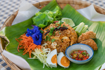 Delicious tom yum fried rice with prawns with salted egg , Fried chicken , top with mango vegetable side dishes Butterfly pea and Chilli Fish Sauce on banana leaf in basket. Thai food style.