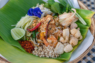 Delicious Fried noodle Thai style with prawns top with peanut lime mango vegetable side dishes Butterfly pea and crackling on banana leaf in basket. Thai food style.