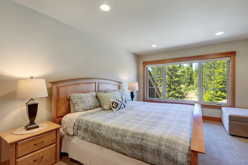 Guest bedroom with wooden bed and great windows with beige carpet. white and blue sheets and huge windows.