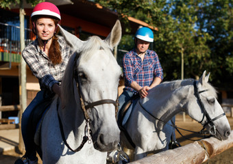 Mature couple in helmets  riding by horse at  barn at summer day