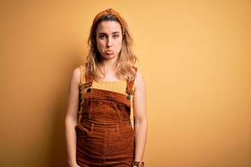 Young beautiful blonde woman wearing overalls and diadem standing over yellow background depressed and worry for distress, crying angry and afraid. Sad expression.