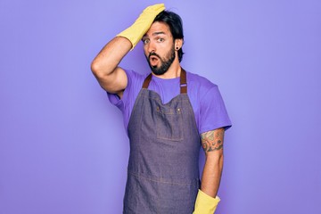 Young handsome hispanic clenaer man wearing housework apron and washing gloves surprised with hand...
