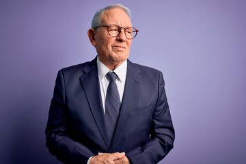 Grey haired senior business man wearing glasses and elegant suit and tie over purple background with hand on stomach because indigestion, painful illness feeling unwell. Ache concept.