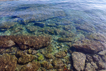 Colorful stones and pebbles are visible through the clear sea water.