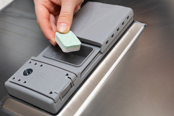 A teenager places a cube of powder in a special dishwasher monument.