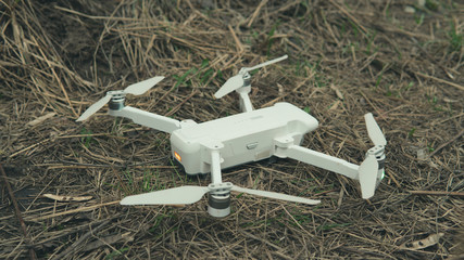 Close-up of white quadrocopter on ground in grass. Modern drone unmanned aerial vehicle with propellers.