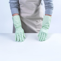 Young woman housekeeper in apron is wearing green gloves to clean the table, concept of preventing virus infection on white background, close up.