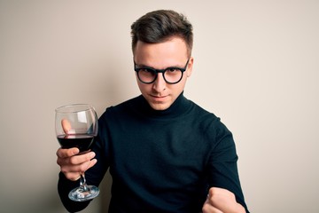 Young handsome caucasian man drinking an alcoholic glass of red wine over isolated background annoyed and frustrated shouting with anger, crazy and yelling with raised hand, anger concept
