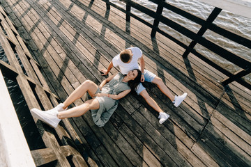 Loving couple sitting on the pier on lake at summer sunset