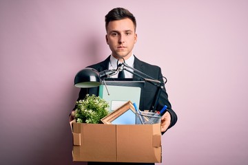 Young handsome caucasian business man holding cardboard box unemployment fired from job with a confident expression on smart face thinking serious - obrazy, fototapety, plakaty