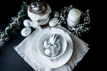 Traditional Easter cake with silver painted eggs, candles and willow on a black background. Selective focus