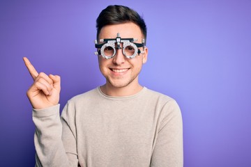 Young handsome caucasian man wearing optometrical glasses over purple background with a big smile on face, pointing with hand and finger to the side looking at the camera.