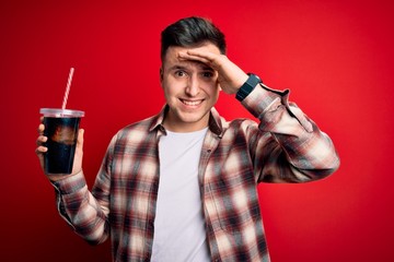Fototapeta na wymiar Young handsome caucasian man drinking a fresh soda refreshment over red background stressed with hand on head, shocked with shame and surprise face, angry and frustrated. Fear and upset for mistake.