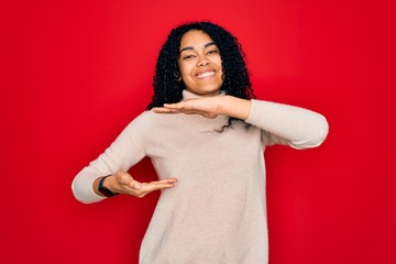 Fototapeta premium Young african american curly woman wearing casual turtleneck sweater over red background gesturing with hands showing big and large size sign, measure symbol. Smiling looking at the camera. Measuring