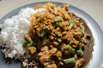 Close up view of pad kra pao, Thai mince meat with green bean and holy basil, with rice on the side.