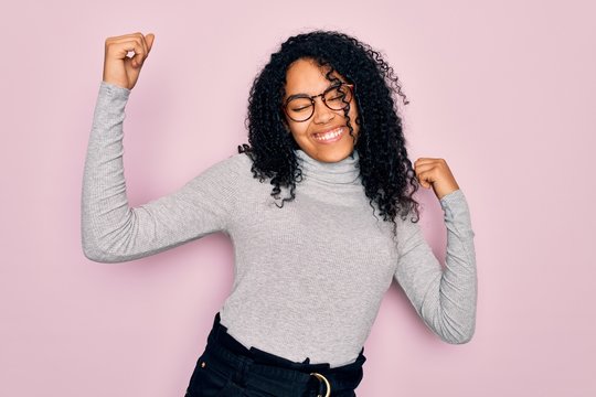 Young african american woman wearing turtleneck sweater and glasses over pink background Dancing happy and cheerful, smiling moving casual and confident listening to music