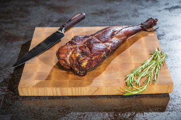 Smoked lamb leg on a wooden board with a knife