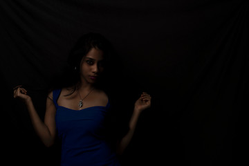 Fashion portrait of an young brunette Indian Bengali woman in vibrant blue western dress in dark studio copy space background. Indian lifestyle and fashion.