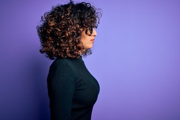 Young beautiful curly arab woman wearing casual sweater and glasses over purple background looking to side, relax profile pose with natural face with confident smile.