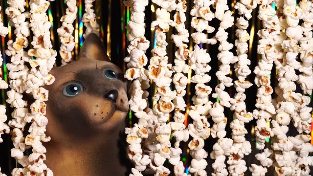 Cat figurine peeked out from garlands of popcorn. Garlands of popcorn for movie news. Invitation to watch movie. Comic news, funny entertainment, fun. 4K video