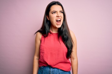 Young brunette woman wearing casual summer shirt over pink isolated background angry and mad screaming frustrated and furious, shouting with anger. Rage and aggressive concept.