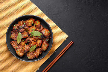 Adobo Pork in black bowl at dark slate background. Pork Adobo or Adobong Baboy is filipino cuisine dish with braised pork belly, bay leaves, soy sauce, vinegar and spices. Filipino food. Top view