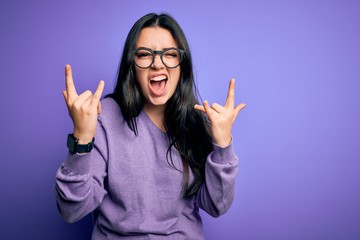 Young brunette woman wearing glasses over purple isolated background shouting with crazy expression...