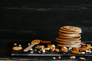 Sweet homemade stack of pancakes with honey filling, almonds and dried apricots, plate on black...