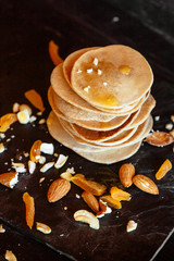 Sweet homemade stack of pancakes with honey filling, almonds and dried apricots, plate on black background. Healthy vegetarian food during quarantine