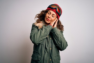 Middle age skier woman wearing snow sportswear and ski goggles over white background sleeping tired dreaming and posing with hands together while smiling with closed eyes.