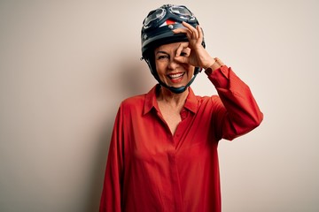 Middle age motorcyclist woman wearing motorcycle helmet over isolated white background doing ok gesture with hand smiling, eye looking through fingers with happy face.