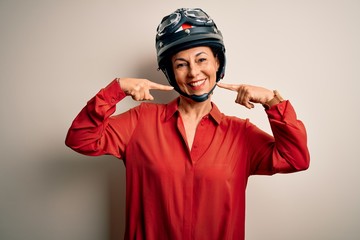 Middle age motorcyclist woman wearing motorcycle helmet over isolated white background smiling cheerful showing and pointing with fingers teeth and mouth. Dental health concept.