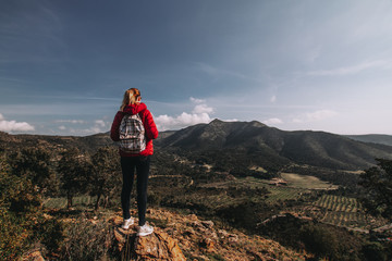 Naklejka premium Young woman enjoying view on mountains in sunset, beautiful nature scenery with mountain tops. Girl or woman traveler with backpack alone, woman travelling solo, view from behind, vacation concept
