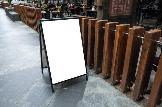 Blank white outdoor advertising stand/sandwich board mock up template. Clear street signage board placed by an outdoor dinning area of a restaurant. Background texture of standee on street.