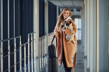 Young female passenger in warm clothes walking with her dog in airport hall