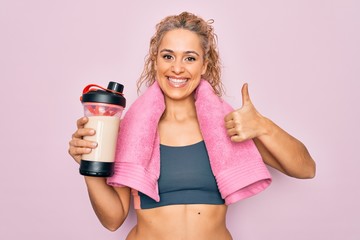 Beautiful blonde sporty woman doing sport wearing towel holding shaker with protein beverage...