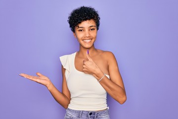 Young beautiful african american afro woman wearing casual t-shirt over purple background Showing palm hand and doing ok gesture with thumbs up, smiling happy and cheerful