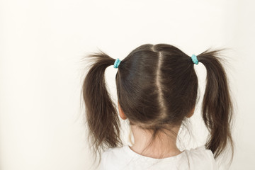 Naklejka premium A girl with two ponytails stands with her back to the camera. The child turned away to the light wall. Upset baby crying
