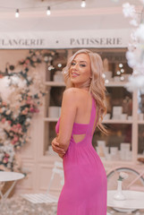 Obraz na płótnie Canvas Attractive smiling blonde in pink sexy dress posing among locations stylized as Paris cafe decorated in pink tones with curly flowers