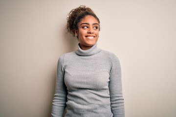 Beautiful african american girl wearing turtleneck sweater standing over white background looking...