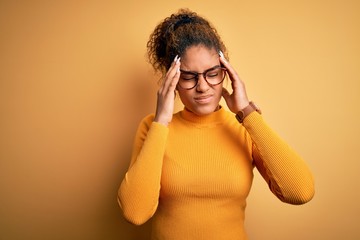 Young beautiful african american girl wearing sweater and glasses over yellow background with hand on headache because stress. Suffering migraine.