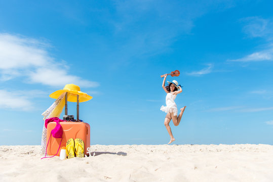 Lifestyle young woman relax on the summer beach.  Asia tourism people jumping and chill in holiday with orange luggage and sunblock items tourist for holiday,  blue sky background.  Summer Concept.