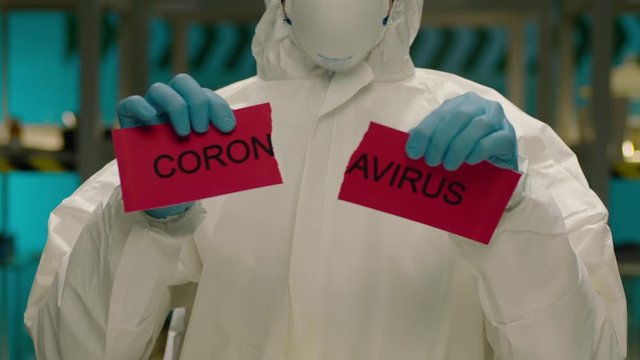 Portrait of masked laborant . Concept of coronavirus quarantine. MERS-Cov. Novel coronavirus. Doctor with a overall safety uniform Tear the red paper with the word coronavirus. COVID-2019 or nCoV2019