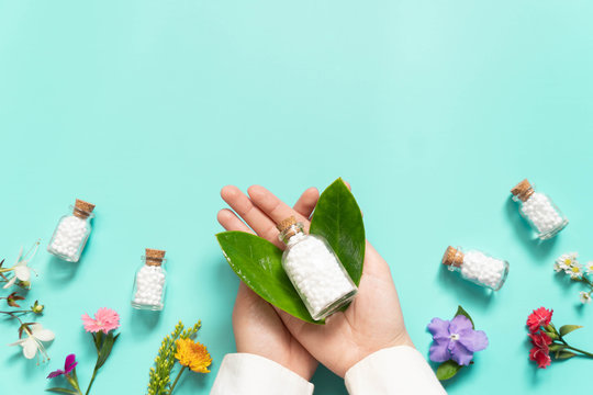 Doctor hands holding homeopathic globules​ bottle with wild flowers​ on green backgound. Homeopathy alternative medicine concept. Flat​ layout. Copy space.
