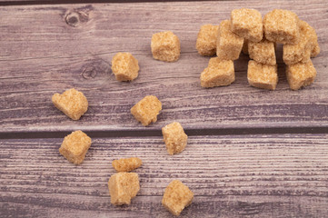 Pieces of brown cane sugar scattered on a wooden background. Close up.